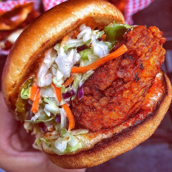 A fried chicken sandwich from 2 Neighbor's, with coleslaw, pickles, and a toasted bun.