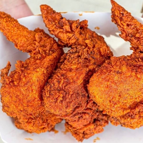 Close-up of several crispy, bright orange fried chicken pieces from 2 Neighbor's in a white container.